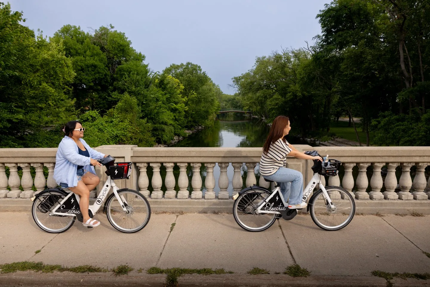 two people riding bike share bicycle across street bridge